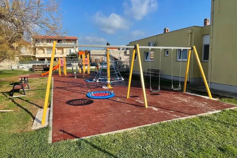Dječje igralište s ljuljačkama i penjalicama uz zgradu vrtića